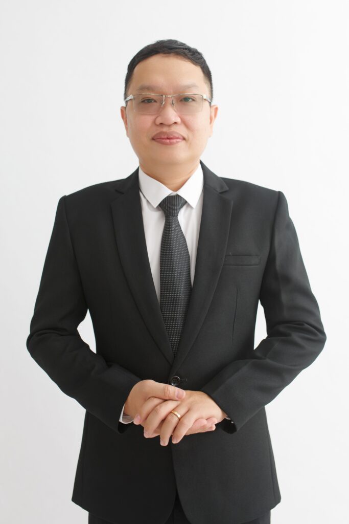 Portrait of a businessman in a black suit standing against a white background, exuding confidence.