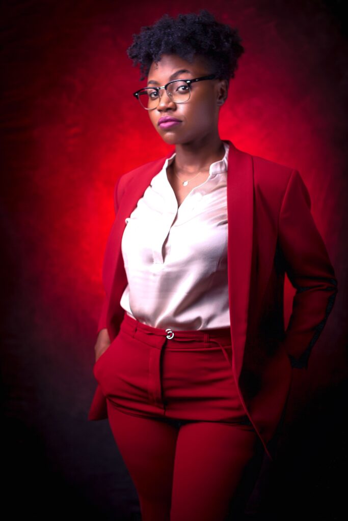 A stylish African American woman poses confidently in a red suit with a striking red backdrop.